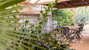 Un espace extérieur aménagé en terrasse, avec une table et des chaises, entouré de verdure et surmonté d’une pergola en bois.