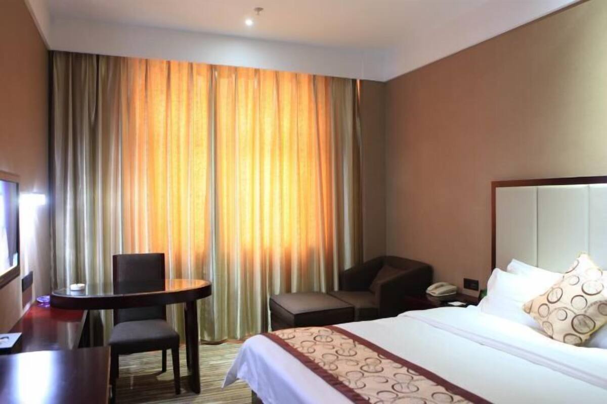 A hotel room with a bed, a desk, a chair, and a small table.
