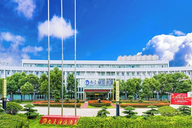 A modern building with a large entrance, surrounded by well-maintained greenery and a clear blue sky.