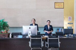 A reception desk with two staff members, a computer, and a plant. - Jiutong Haiyuan International Hotel (Wuhan)