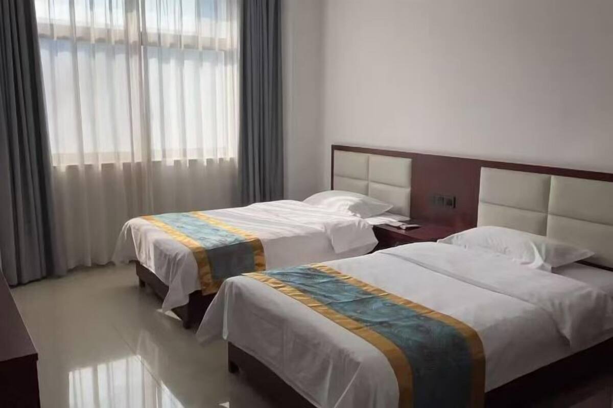A hotel room with two beds, a wooden headboard, and a large window with curtains.
