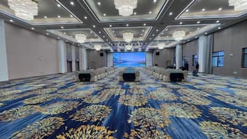 Uma grande sala de conferências com carpete estampado, fileiras de mesas e um palco na frente.