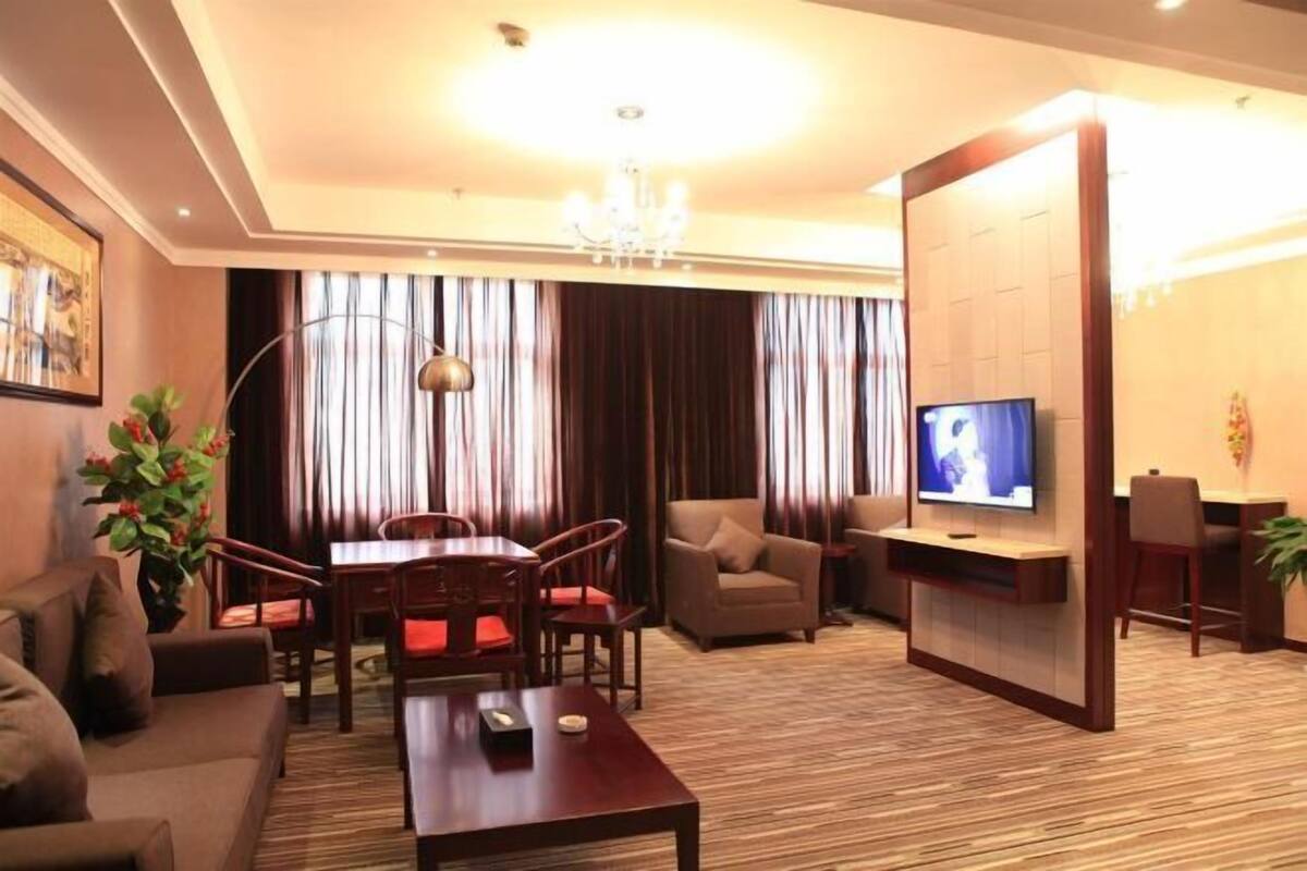 A hotel room with a sofa, a dining table with chairs, a TV, and a desk.