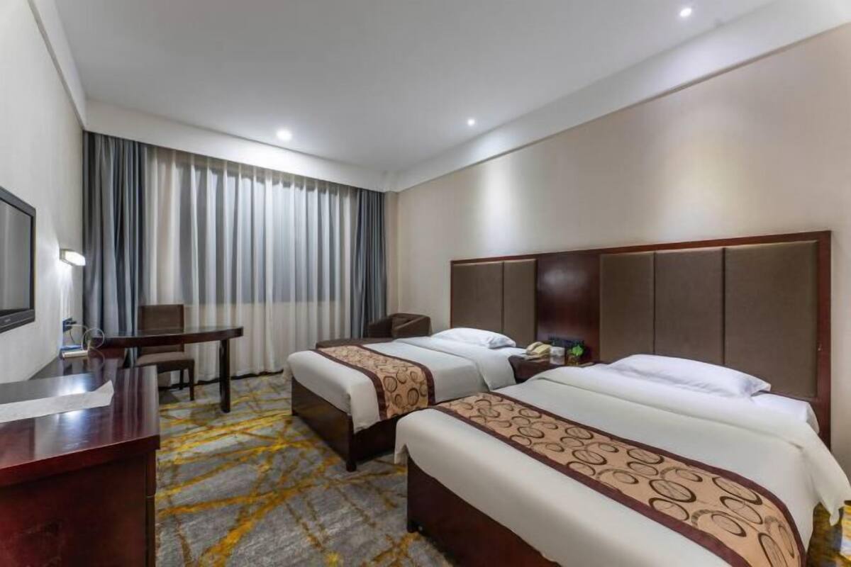 A hotel room with two beds, a desk, a chair, and a TV.