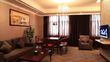 A hotel room with a sofa, a dining table with chairs, a TV, and a chandelier.