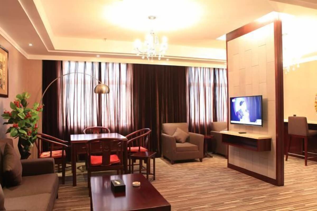 A hotel room with a dining table, chairs, a sofa, a TV, and a chandelier.