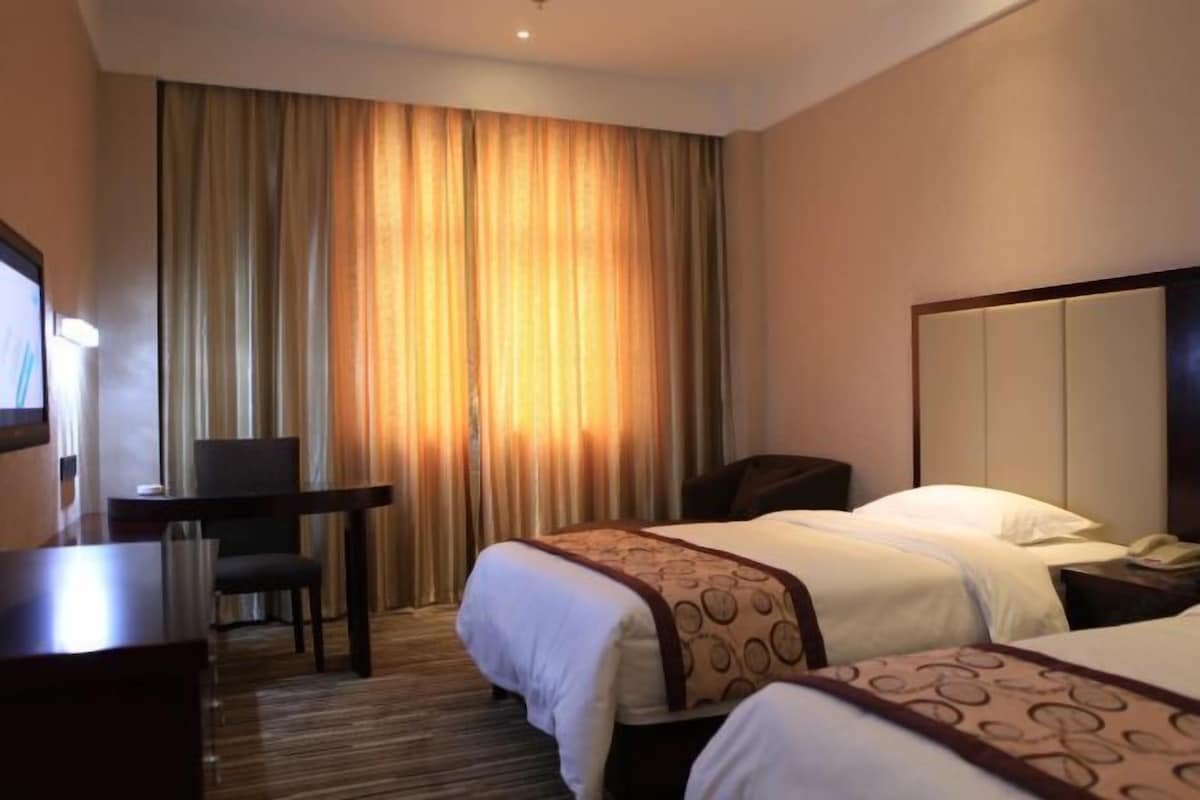 A hotel room with two beds, a desk, and a chair.