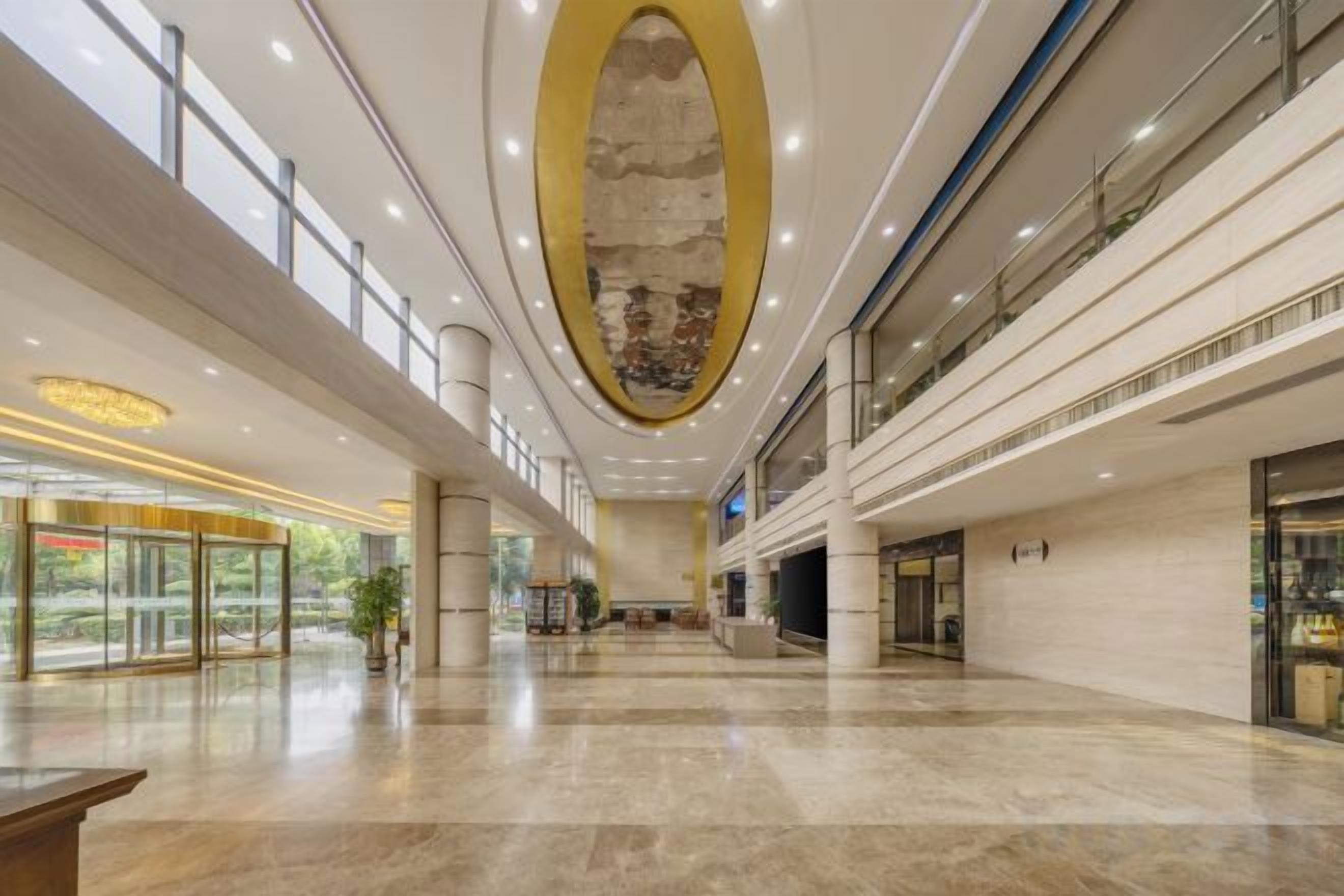 Un hall d’entrée spacieux avec un plafond haut, des rampes en verre et une colonne centrale.