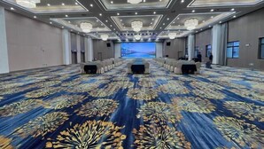 A large conference room with a patterned carpet, multiple tables, and a large screen at the front. - Jiutong Haiyuan International Hotel (Wuhan)