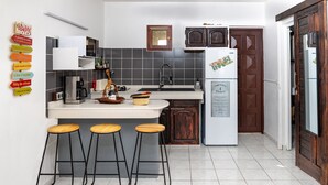 A modern kitchen with a central island, bar stools, a refrigerator, and a tiled backsplash. - Gîtes Papillon - Studio with swimming pool (Saint-François)