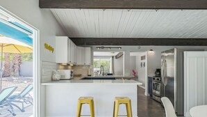 A modern kitchen with a central island, stainless steel appliances, and a view to the outdoors. - Quintessential Midcentury Modern Alexander House (Palm Springs)