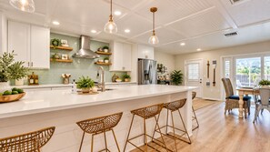 A modern kitchen with white cabinetry, a stainless steel range hood, and a large island with bar stools. - STUNNING! Game Room, Pool, Beaches & Full Remodel! (Bradenton)