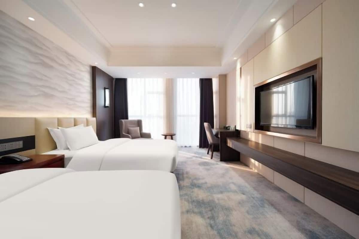 A hotel room with two beds, a TV mounted on the wall, a desk, and a chair.