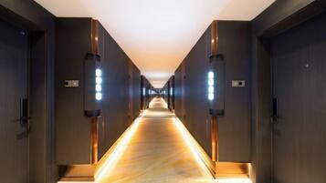 A long, narrow hotel corridor with doors on both sides and illuminated by wall-mounted lights.