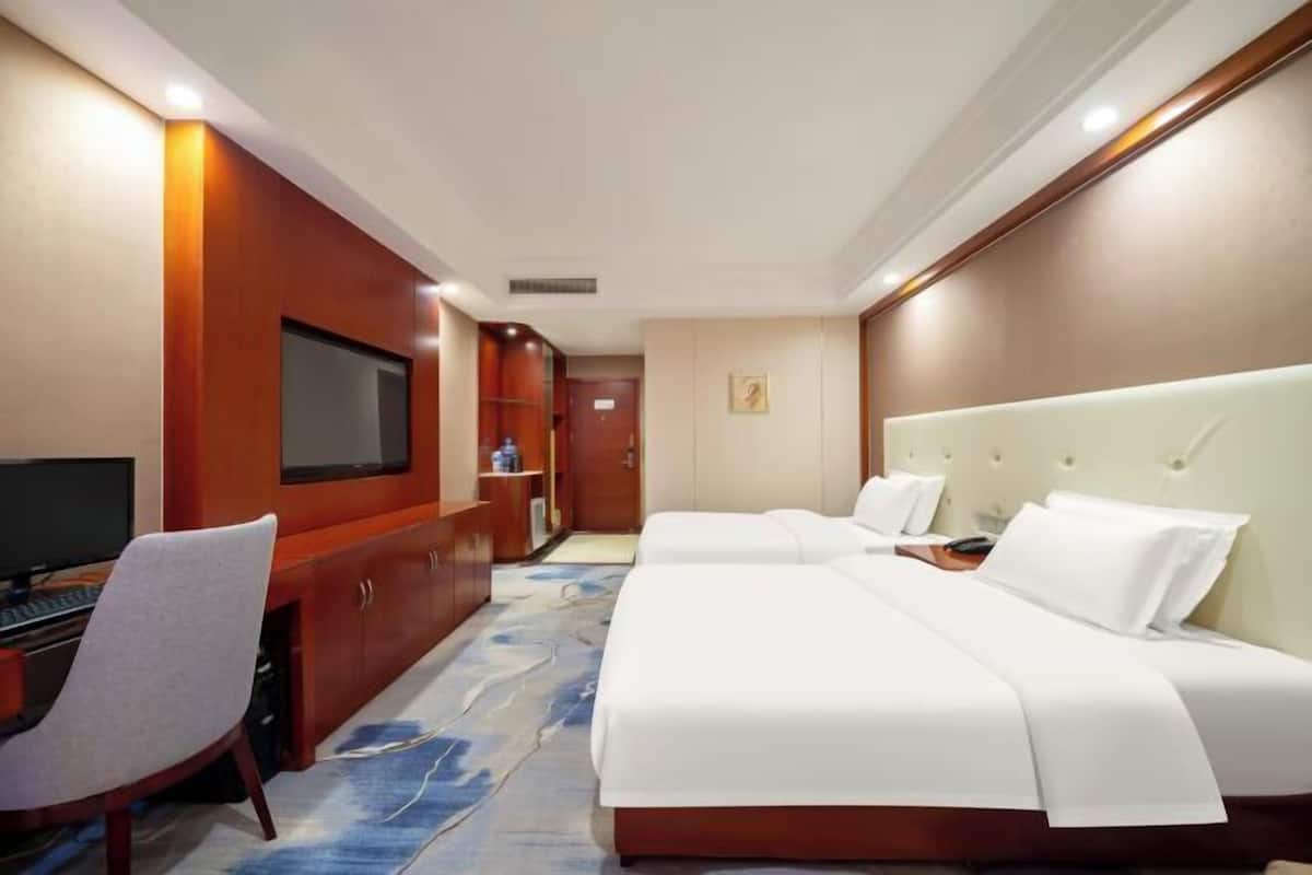 A hotel room with two beds, a desk with a computer, a TV, and a minibar.