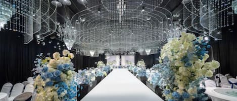 Un long couloir étroit au sol blanc, bordé de rangées de chaises blanches et agrémenté de compositions florales aux motifs bleus et blancs.