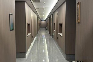 Un pasillo de hotel con puertas a ambos lados, un suelo brillante e iluminación empotrada.
