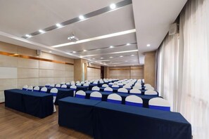 Un salón de conferencias con filas de mesas y sillas, un proyector y un ventanal grande.