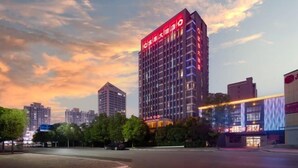Un hotel moderno a grattacielo con insegne illuminate, circondato da altri edifici e alberi.