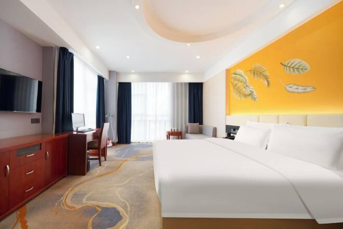 A hotel room with a large bed, a desk, a TV, and a wall with leaf patterns.