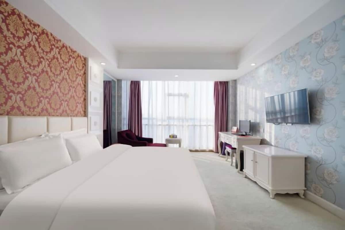 A hotel room with a large bed, a desk, a TV, and a view of the city.