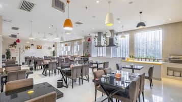 A spacious restaurant with multiple tables and chairs, pendant lighting, and large windows.