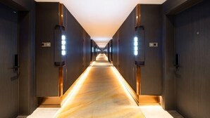 Un corridoio moderno di un albergo con un percorso illuminato al centro, pareti scure e porte su entrambi i lati.