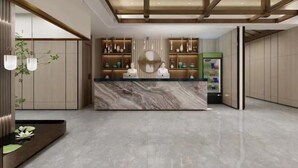 Una hall d'albergo moderna con una reception in marmo, lampade a sospensione e una macchina distributrice verde.