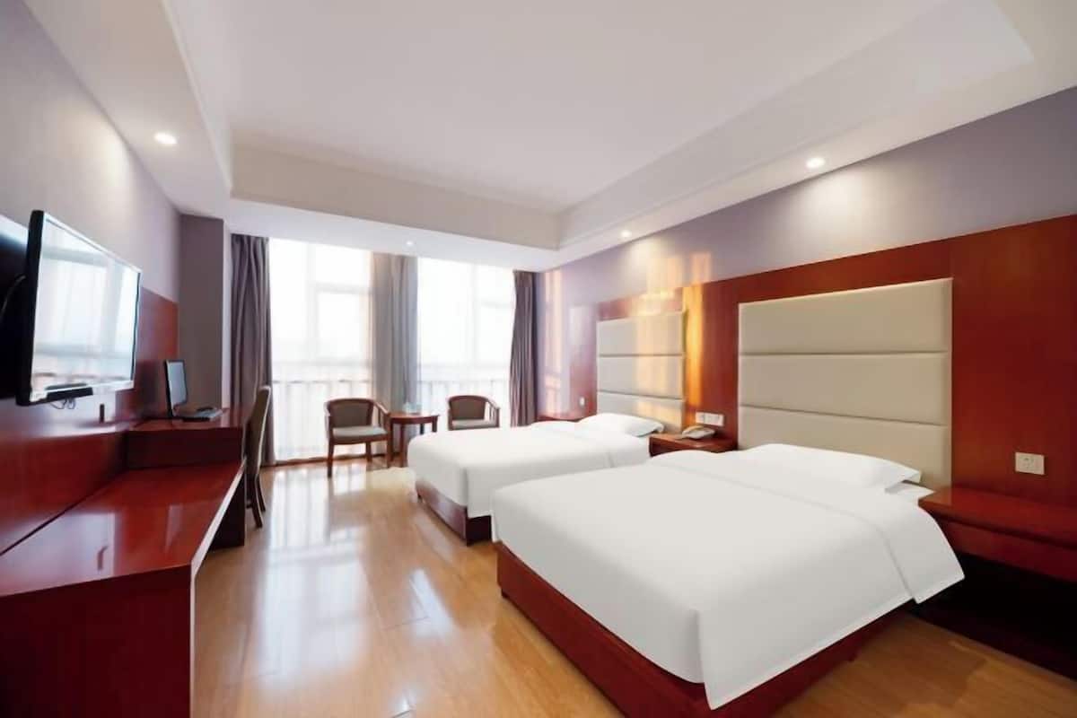 A hotel room with two beds, a desk, a TV, and a seating area.