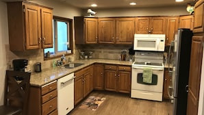 Una cocina con armarios de madera, un microondas, un refrigerador, un lavavajillas y un fregadero.