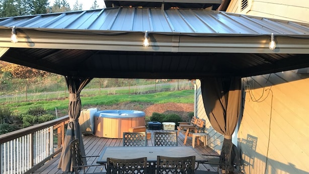 Una terraza exterior con zona de estar cubierta, un jacuzzi y una mesa de madera con sillas.