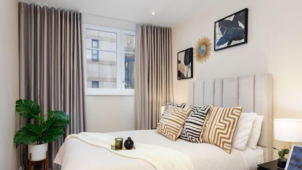 A bedroom with a large bed, a bedside table with a lamp, a potted plant, and a window with curtains. - Chancery Lane, Central London by Interhome (London City)