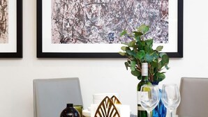 A dining table with a glass top, a bottle of wine, two wine glasses, a decorative plant, and framed artwork on the wall. - Chancery Lane, Central London by Interhome (London City)