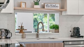 A modern kitchen with a stainless steel sink, wooden cabinets, a coffee maker, and a window with a view of greenery. - Lakefront Oasis In Hollywood | Hard rock casino (Fort Lauderdale)