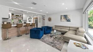 A modern living room with a sofa, blue armchairs, a coffee table, and a kitchen area in the background. - Lakefront Oasis In Hollywood | Hard rock casino (Fort Lauderdale)