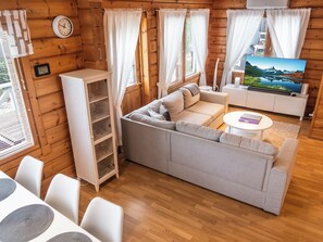 Interior acolhedor de uma cabana com sofá, televisão, área de jantar e paredes de madeira.