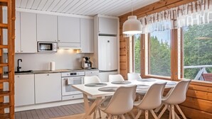 A modern kitchen with white cabinets, a dining table with chairs, and a view of greenery outside.