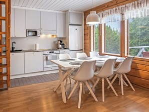 A modern kitchen with white cabinetry, a dining table with chairs, and a view through large windows.