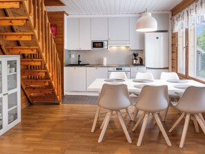 A modern kitchen with white cabinets, a microwave, and a coffee maker. There is a dining table with chairs and a staircase with wooden railings. - Vuokatin molle by Interhome (Sotkamo)