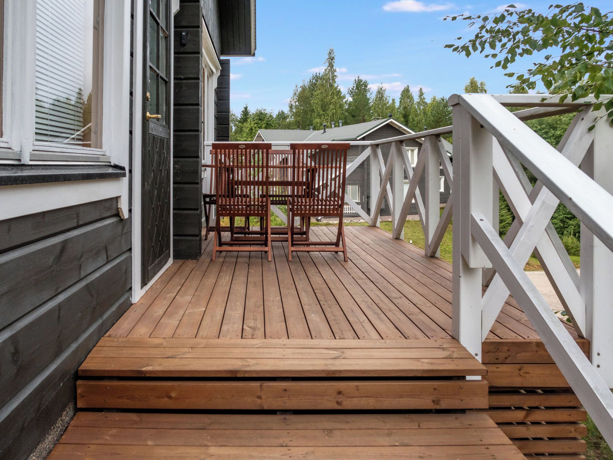 Une terrasse en bois avec deux chaises en bois et une rambarde blanche.