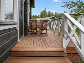 Een houten terras met twee houten stoelen en een witte balustrade.