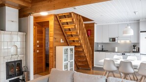 A cozy living room with a sofa, a fireplace, and a kitchen area with white cabinets and a wooden staircase.