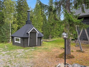 A small cabin with a chimney, surrounded by trees and a swing set.