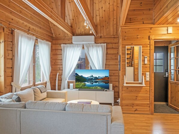 A wooden cabin interior with a sofa, a flat-screen TV, and a door leading to a bathroom.