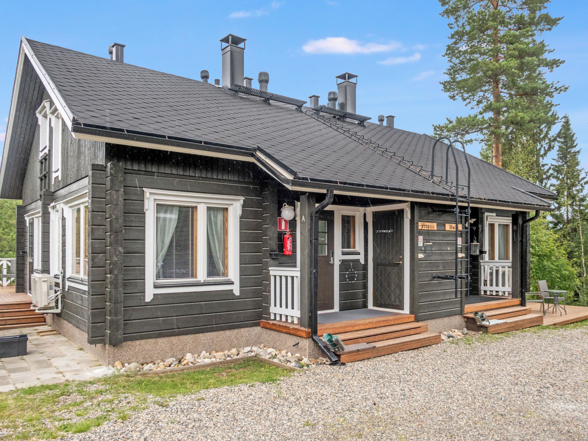 Une cabane en rondins à deux étages, avec une façade sombre, des boiseries blanches et un porche à l’avant.