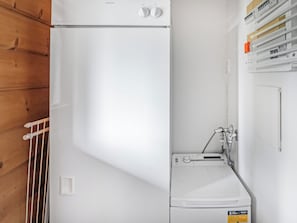 Een kleine wasruimte met een wasmachine en droger, een houten wand en een metalen rek.
