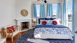 A bedroom with a bed, a fireplace, a ceiling fan, and large windows with curtains. - High Style, Fun Decor, Awesome Location! 117D by Forsyth Park (Savannah)