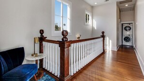 A spacious hallway with a wooden railing, a blue chair, and a washing machine in the background. - High Style, Fun Decor, Awesome Location! 117D by Forsyth Park (Savannah)