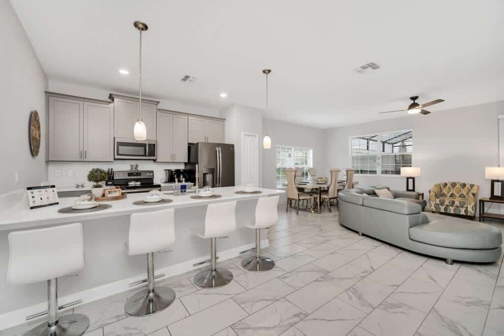 A modern kitchen with a central island, bar stools, and a dining area with a sofa and chairs.