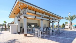 Un espace extérieur abrité, doté de chaises et de tables, un bâtiment avec un toit en tuiles et un ciel dégagé.